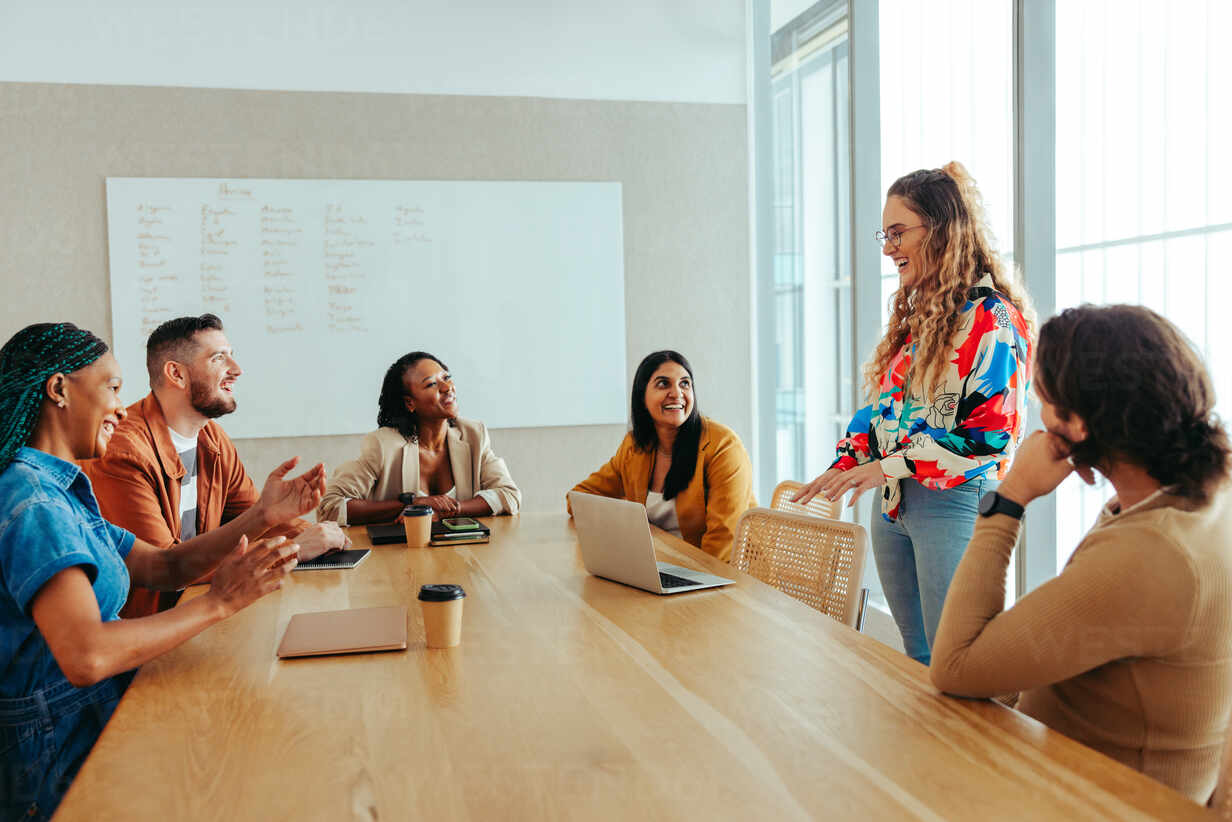 A diverse group of digital marketing professionals engaged in a meeting. The team is discussing strategies and ideas in an open, collaborative environment around a wooden table in a bright office.
